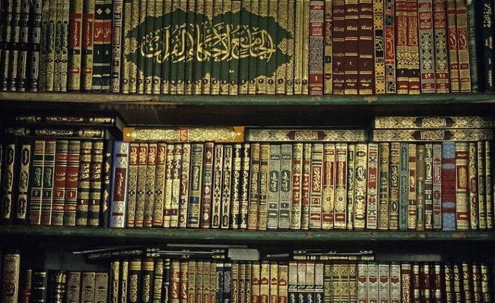 Shelves of Arabic books with gold-lettered spines in green, red and teal bindings.